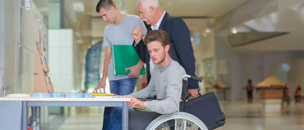 Schüler im Rollstuhl mit Mitschüler und Lehrer auf einer Berufsmesse.